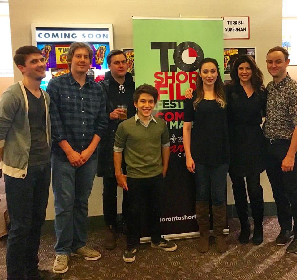 Seven people stand in a line in a cinema lobby in front of a T.O Short Film Festival pull-up banner, with film posters on the wall behind them.
