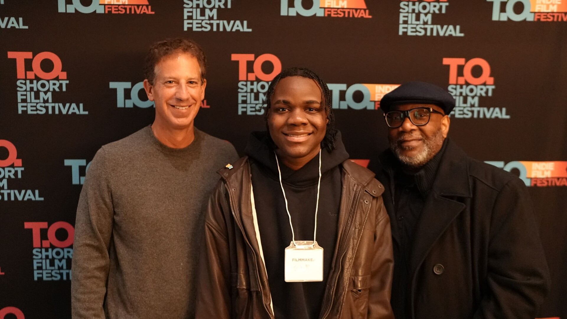 Three filmmakers pose together in front of a T.O Short Film Festival backdrop.