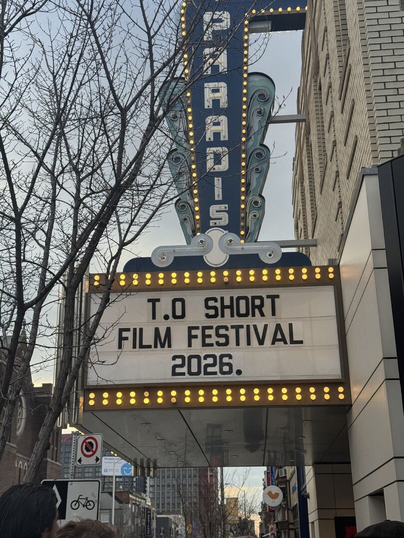 The Paradise Cinema's vertical neon blade sign and marquee board reading T.O Short Film Festival 2026, seen from below against bare trees and an overcast sky.